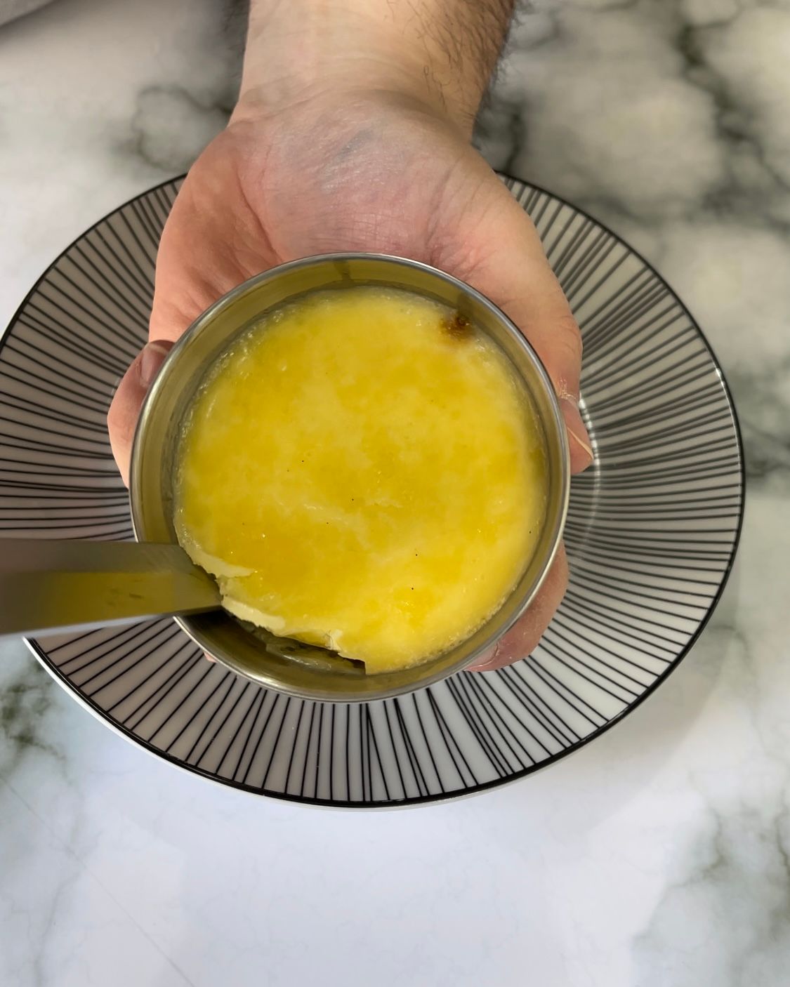 Una persona tiene in mano un misurino contenente un liquido giallo su un piatto.