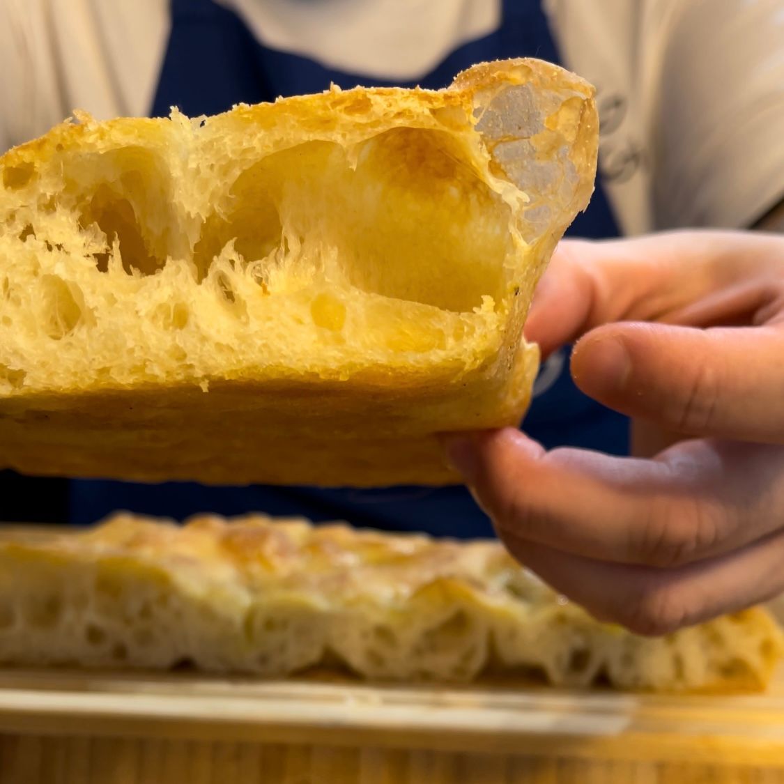 Fetta di focaccia alta e soffice servita tiepida, mostra l'alveolatura