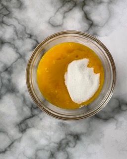 Una ciotola di vetro piena di liquido giallo e zucchero bianco su un tavolo.