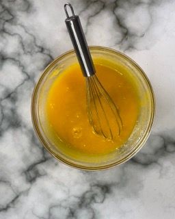 Una ciotola di liquido giallo con una frusta dentro.