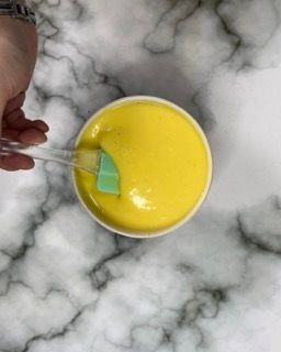 Una persona sta mescolando un liquido giallo in una ciotola con una spatola.