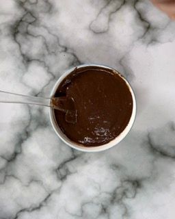 Una ciotola di salsa al cioccolato con un cucchiaio dentro su un tavolo.