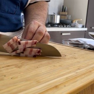 Un uomo sta tagliando la pancetta su un tagliere di legno