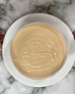 Una ciotola di salsa è su un piatto bianco su un tavolo.