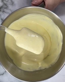 Una persona sta mescolando un liquido giallo in una ciotola di metallo con una spatola.