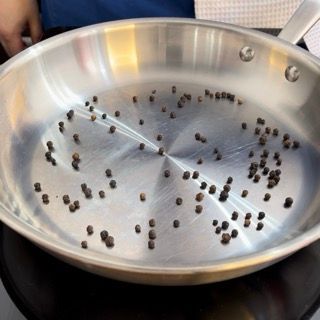 Una padella d'argento piena di grani di pepe nero