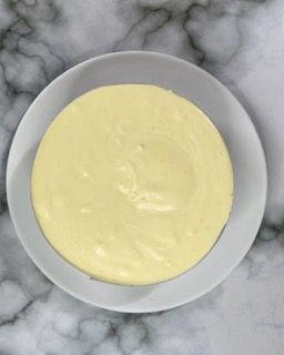 Una ciotola bianca piena di salsa gialla su una superficie di marmo.