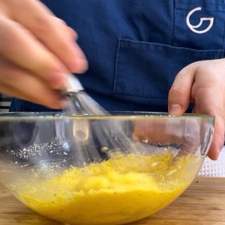 Una persona sta mescolando un liquido giallo in una ciotola di vetro.