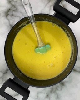 Una pentola di zuppa gialla con dentro una spatola verde.