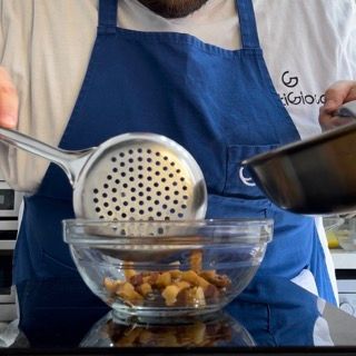Un uomo con un grembiule blu tiene uno scolapasta sopra una ciotola di cibo
