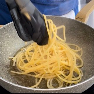 Una persona tiene un paio di pinze sopra una padella di spaghetti