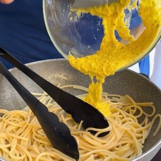 Una persona sta versando la salsa gialla in una padella di spaghetti