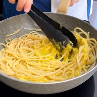 Una persona sta mescolando gli spaghetti in una padella con le pinze