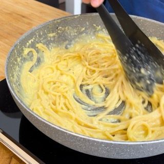 Una persona sta mescolando gli spaghetti in una padella con le pinze.