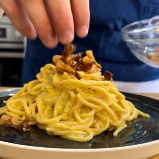 Una persona aggiunge funghi a un piatto di spaghetti