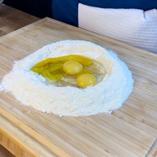 Un tagliere di legno con sopra farina e uova