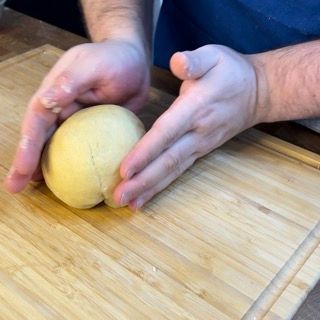 Una persona tiene in mano una palla di pasta su un tagliere