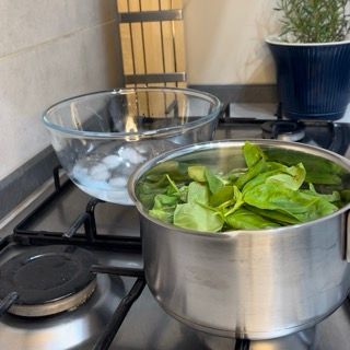 Una pentola di spinaci sta cuocendo su un fornello accanto a una ciotola di ghiaccio