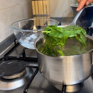 Una persona sta cucinando gli spinaci in una pentola sul fornello
