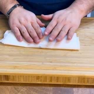 Una persona si pulisce le mani con un tovagliolo su un tagliere di legno