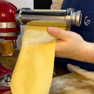 Una persona sta usando una macchina per la pasta con la lettera g sul grembiule