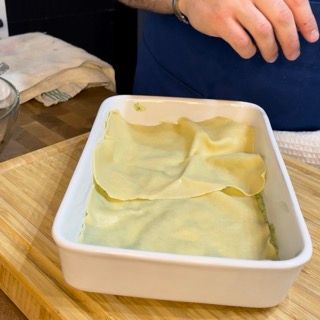 Una casseruola bianca piena di tagliatelle su un tagliere di legno