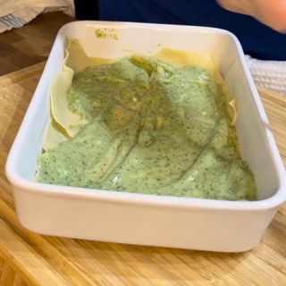 Una casseruola bianca piena di salsa verde su un tavolo di legno