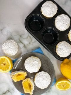 Uno stampo per muffin pieno di ciambelle ricoperte di zucchero a velo accanto a un piatto di ciambelle e limoni.