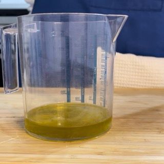 Un misurino pieno di liquido è appoggiato su un tavolo di legno.