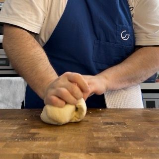 Un uomo con un grembiule blu sta impastando la pasta su un tagliere