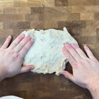 Una persona tiene in mano un pezzo di pasta su un tagliere di legno