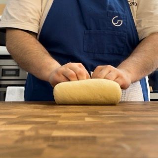 Un uomo con un grembiule blu sta impastando la pasta