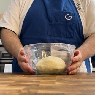 Un uomo con un grembiule blu tiene in mano una ciotola di pasta
