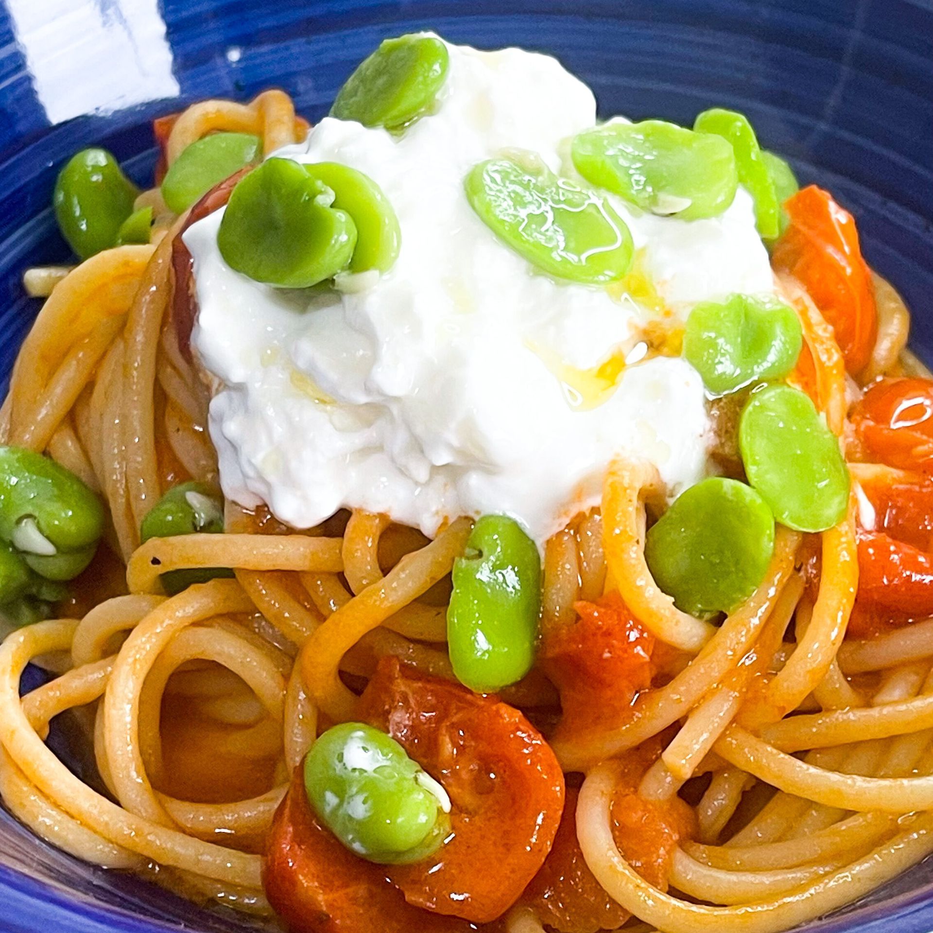 Una ciotola blu piena di spaghetti pomodori e fagiolini