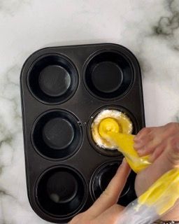 Una persona sta versando la glassa gialla in uno stampo per muffin.