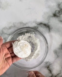 Una persona tiene in mano un biscotto sopra una ciotola di zucchero a velo.