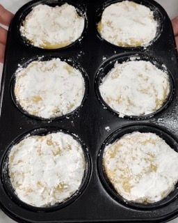 Una persona tiene in mano uno stampo per muffin pieno di cupcakes ricoperti di zucchero a velo