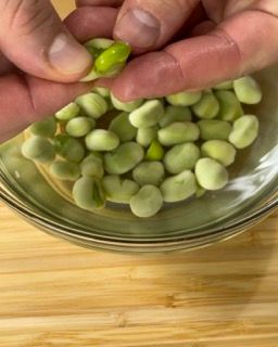 Una persona tiene in mano un fagiolino sopra una ciotola di fagiolini.