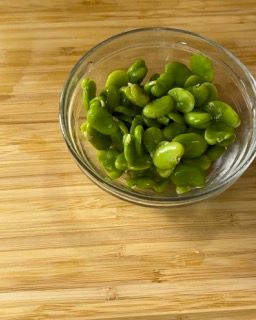 Una ciotola di vetro piena di fagiolini su un tavolo di legno.