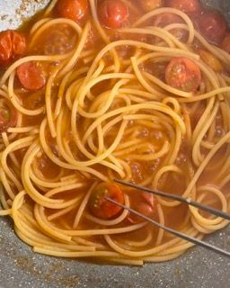 Gli spaghetti e i pomodori vengono cotti in una padella con le pinze.