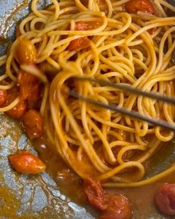 Un primo piano di spaghetti e pomodori in una padella con pinze.