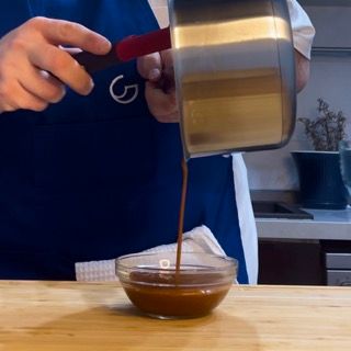 Una persona che versa la salsa in una ciotola con la lettera g sul grembiule