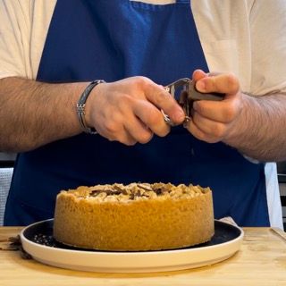 Un uomo con un grembiule sta tagliando una torta con un paio di forbici