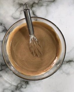 Una ciotola di liquido marrone con una frusta dentro