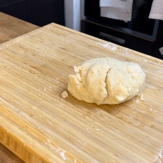 Una palla di pasta è appoggiata su un tagliere di legno.