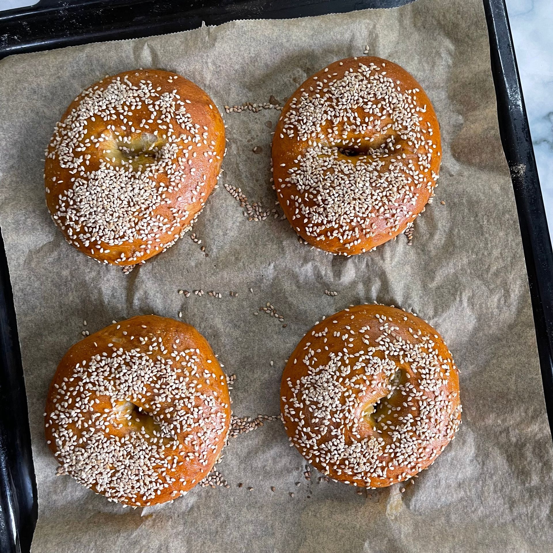 Quattro bagel ricoperti di semi di sesamo sono adagiati su una teglia da forno.