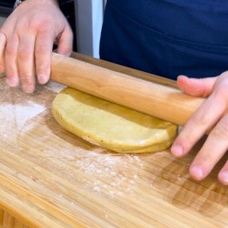 Una persona sta stendendo la pasta con un mattarello su un tagliere di legno.