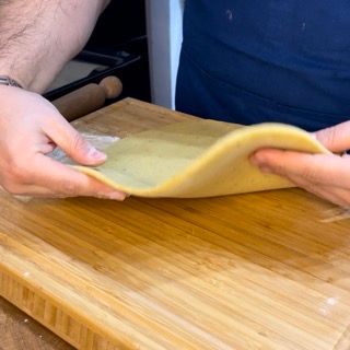 Una persona tiene in mano un pezzo di pasta su un tagliere di legno.