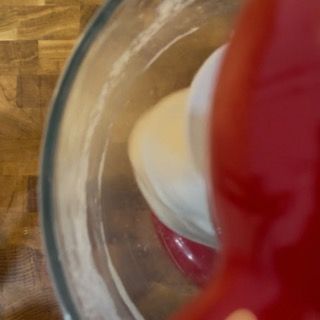 Una persona sta mescolando qualcosa in una ciotola di vetro con un coperchio rosso.