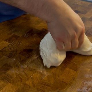 Una persona sta impastando l'impasto su un tagliere di legno.